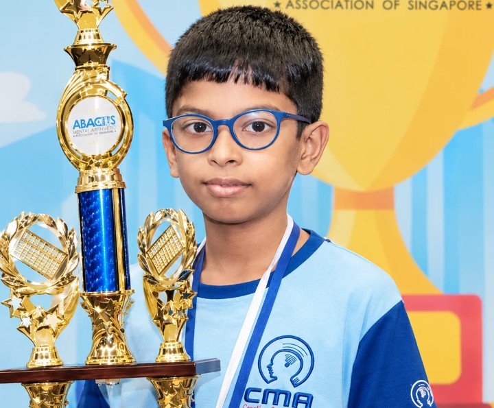 A young CMA student in his CMA T-shirt standing with a large trophy