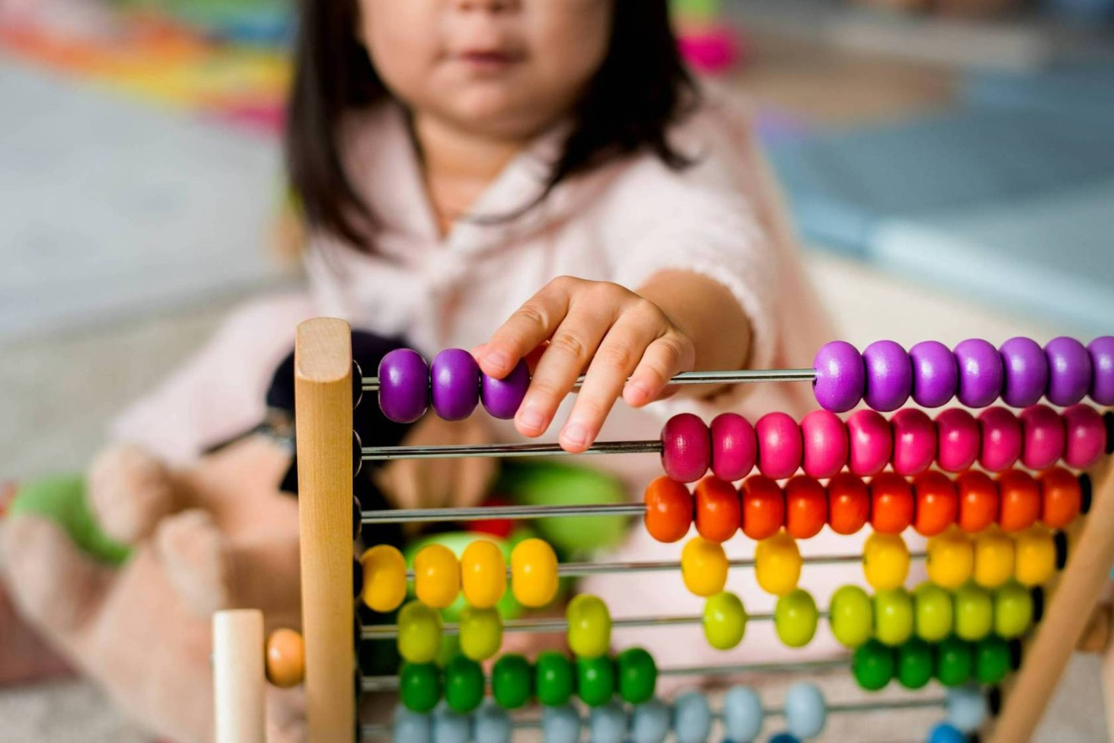 A young child moving colourful beads on a rainbow abacus