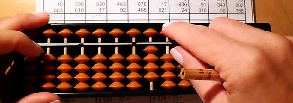 Hands working out sums on a soroban abacus over a practice worksheet