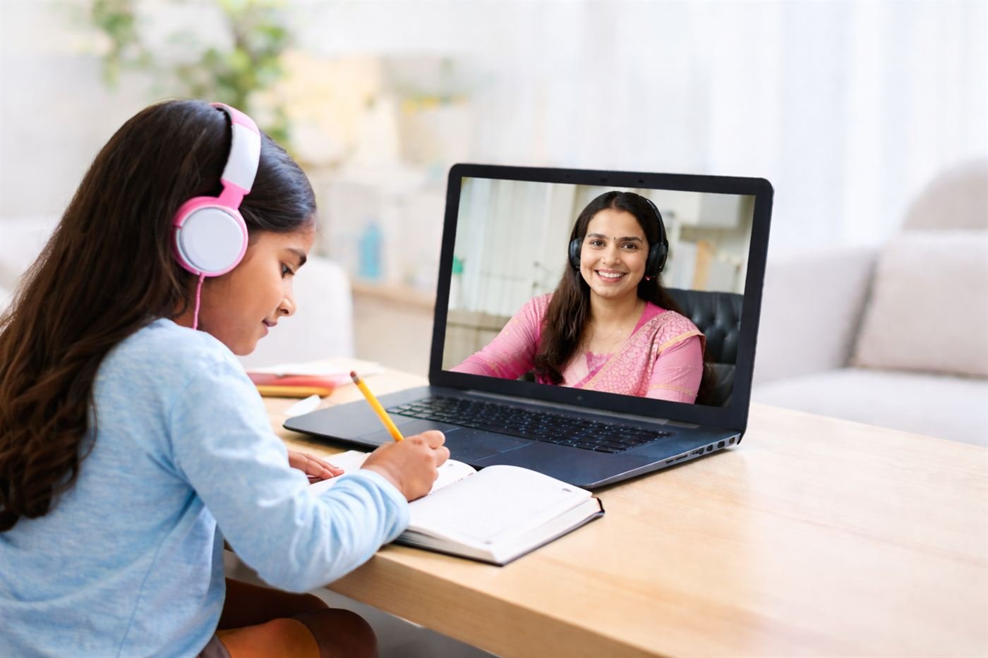 A girl with headphones taking notes during a live online lesson with her teacher